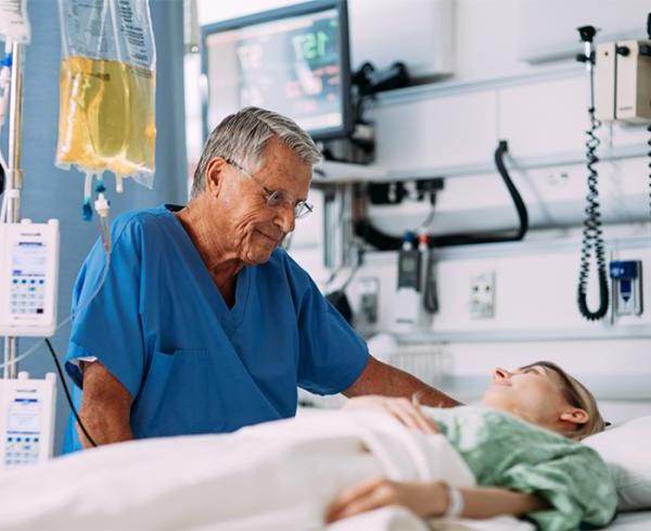医疗保健专业人员在床边与病人互动. 背景中显示的是静脉输液袋和输液泵.